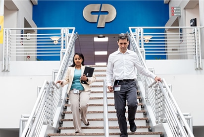 Zamestnanci spoločnosti Colgate-Palmolive schádzajú po schodoch, za nimi je na modrej stene logo spoločnosti Colgate-Palmolive.