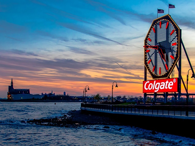 pobrežie, logo Colgate v pozadí pod veľkými hodinami s červenými ručičkami